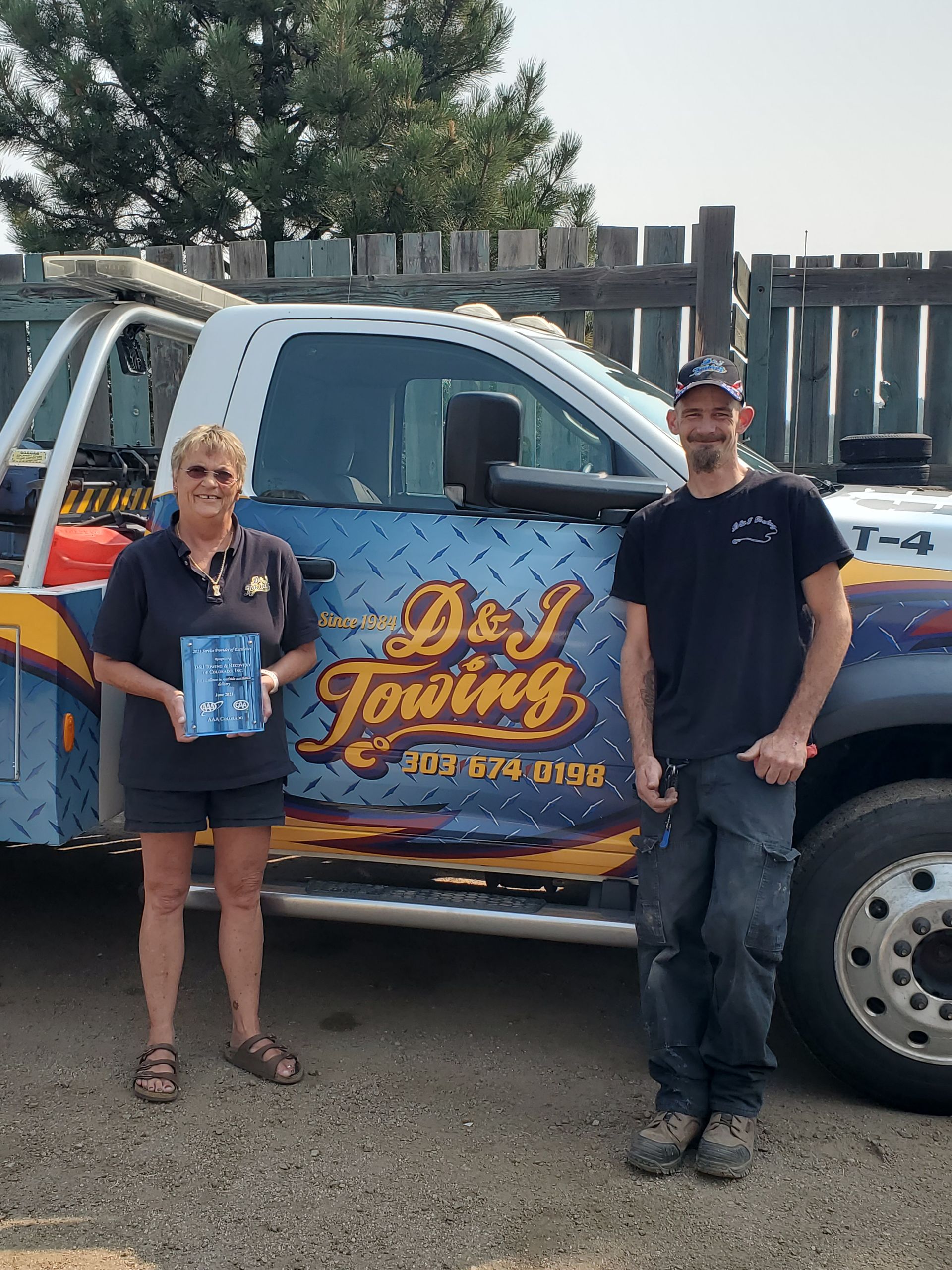 A D&J team member holding a plaque beside the D&J logo on a tow truck door