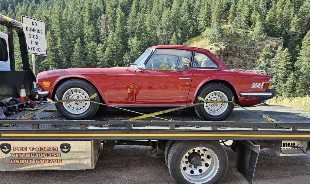 Red classic convertible secured on a flatbed with pine forest behind