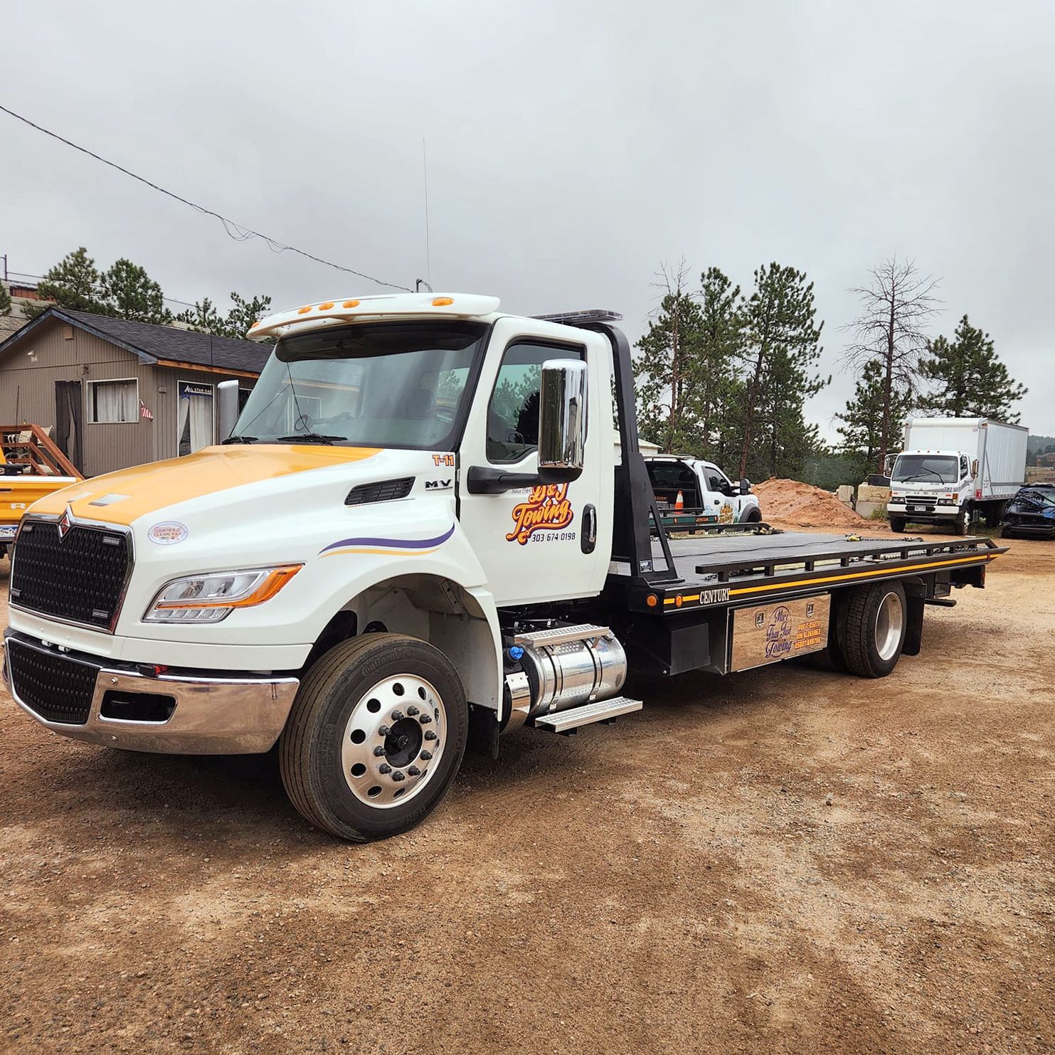 D&J Towing flatbed rollback truck parked at the Evergreen yard with pine trees behind