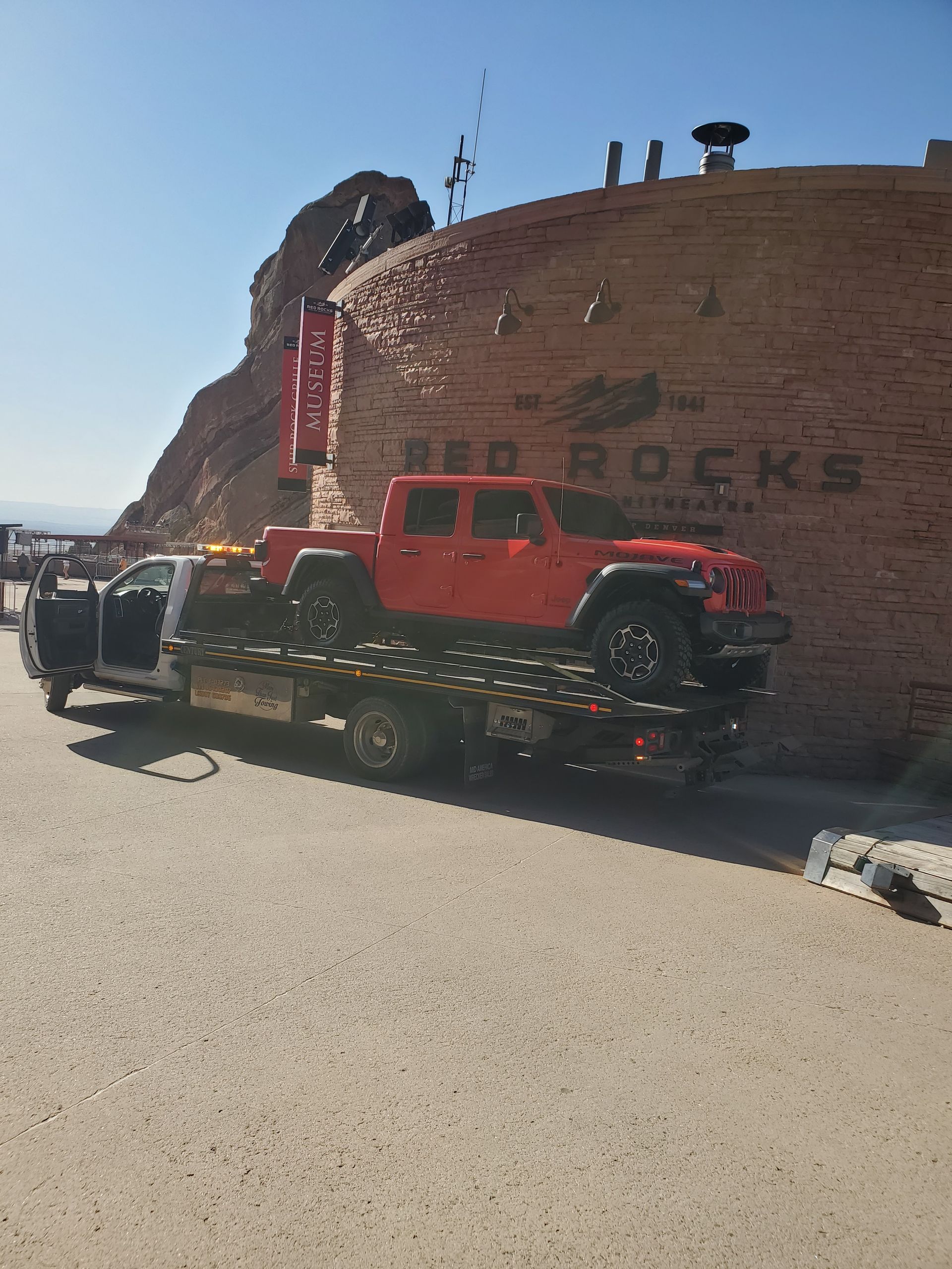 Red Jeep Gladiator strapped on a D&J flatbed in front of a Red Rocks sign