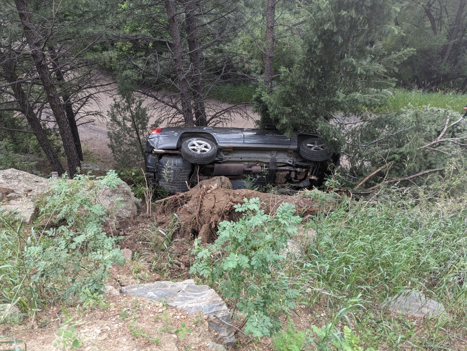 Vehicle on its side in the trees off a mountain road before recovery
