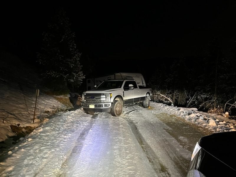Pickup on a snow-covered road at night lit by work lights